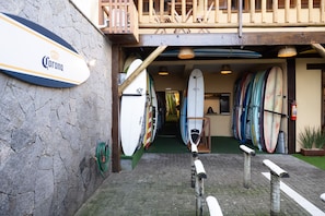 Una tienda de alquiler de tablas de surf con un letrero de Corona, tablas de surf y un balcón de madera.