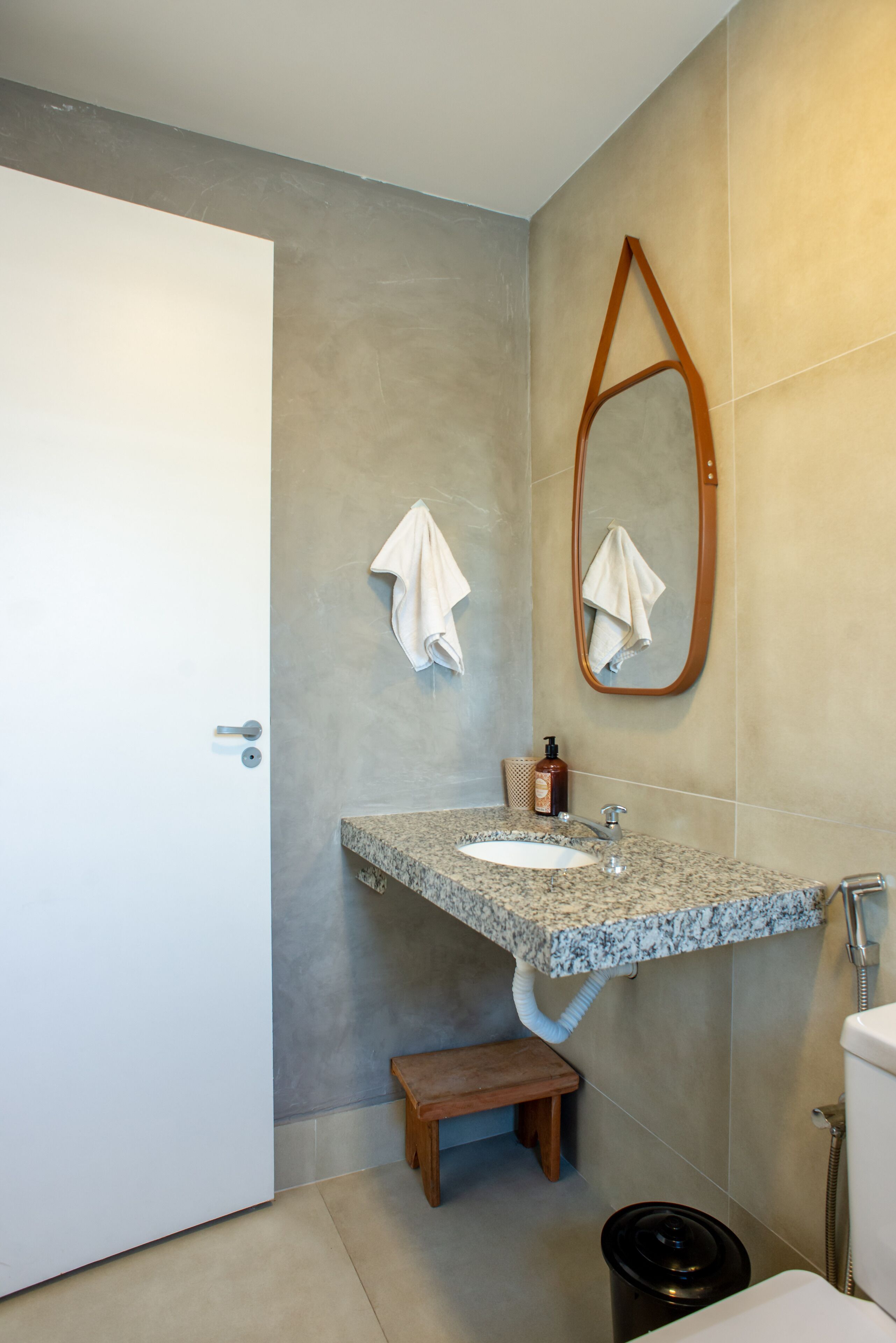 Een badkamer met een wastafel op een granieten blad, een houten bankje, een toilet en een spiegel met houten lijst.