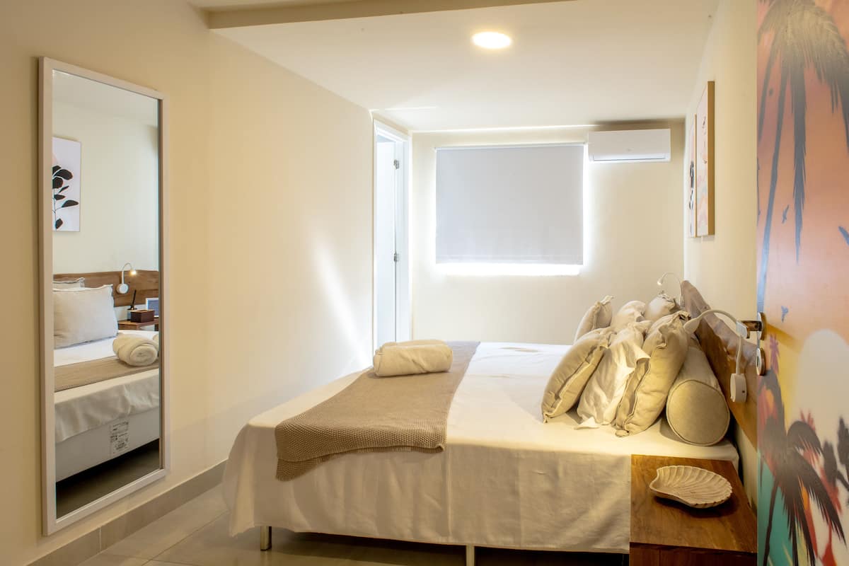 Um quarto com uma cama, mesa de cabeceira, espelho e janela.