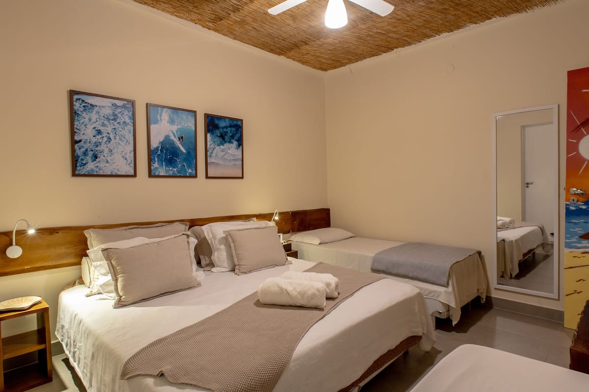 Quarto de hotel com duas camas, teto de madeira e três quadros na parede.