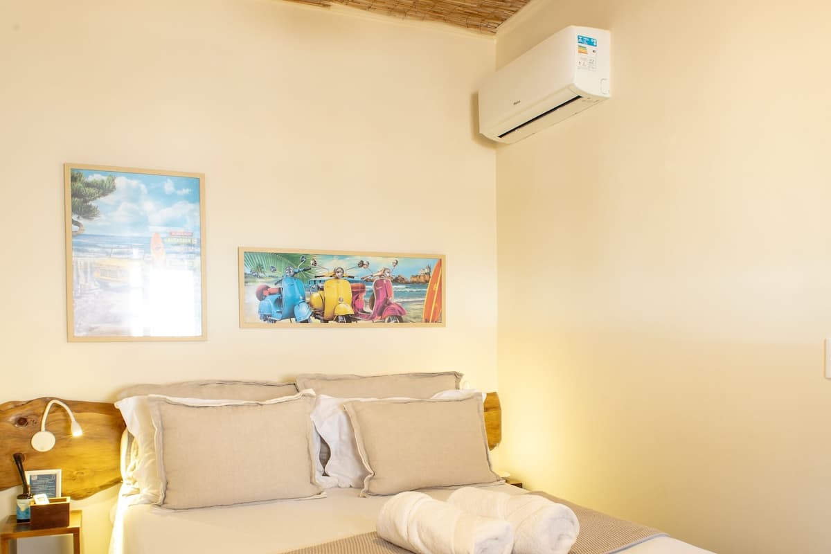 Quarto com cama, ventoinha no teto, aparelho de ar condicionado e duas imagens emolduradas na parede.