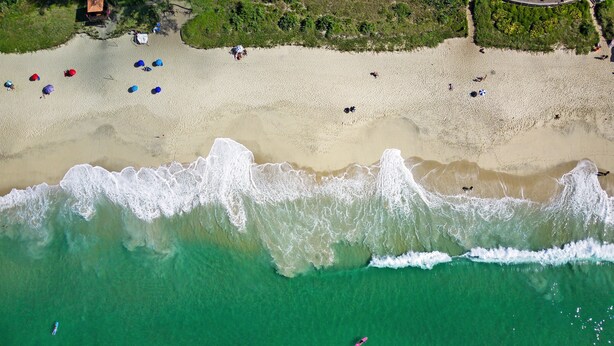 Vista aérea de una playa con aguas turquesas cristalinas, una orilla arenosa y algunas sombrillas y personas.