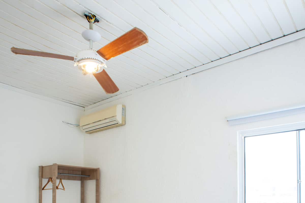 Uma cama bem arrumada com um cobertor marrom, cabeceira de madeira e ventilador de teto.