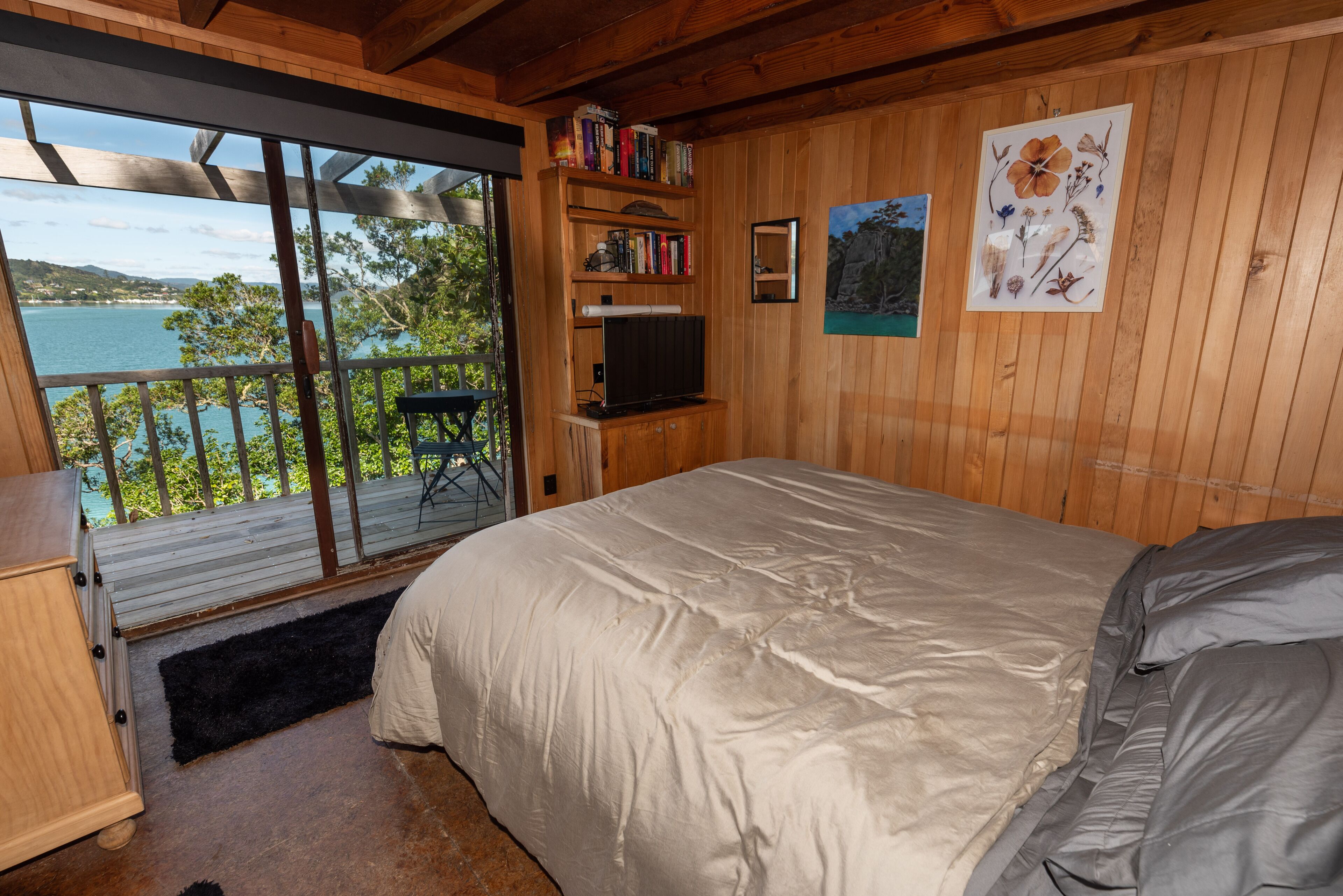 Una camera da letto con un letto grande, pareti in legno, una libreria, una TV a parete e vista su un lago tramite una porta scorrevole.