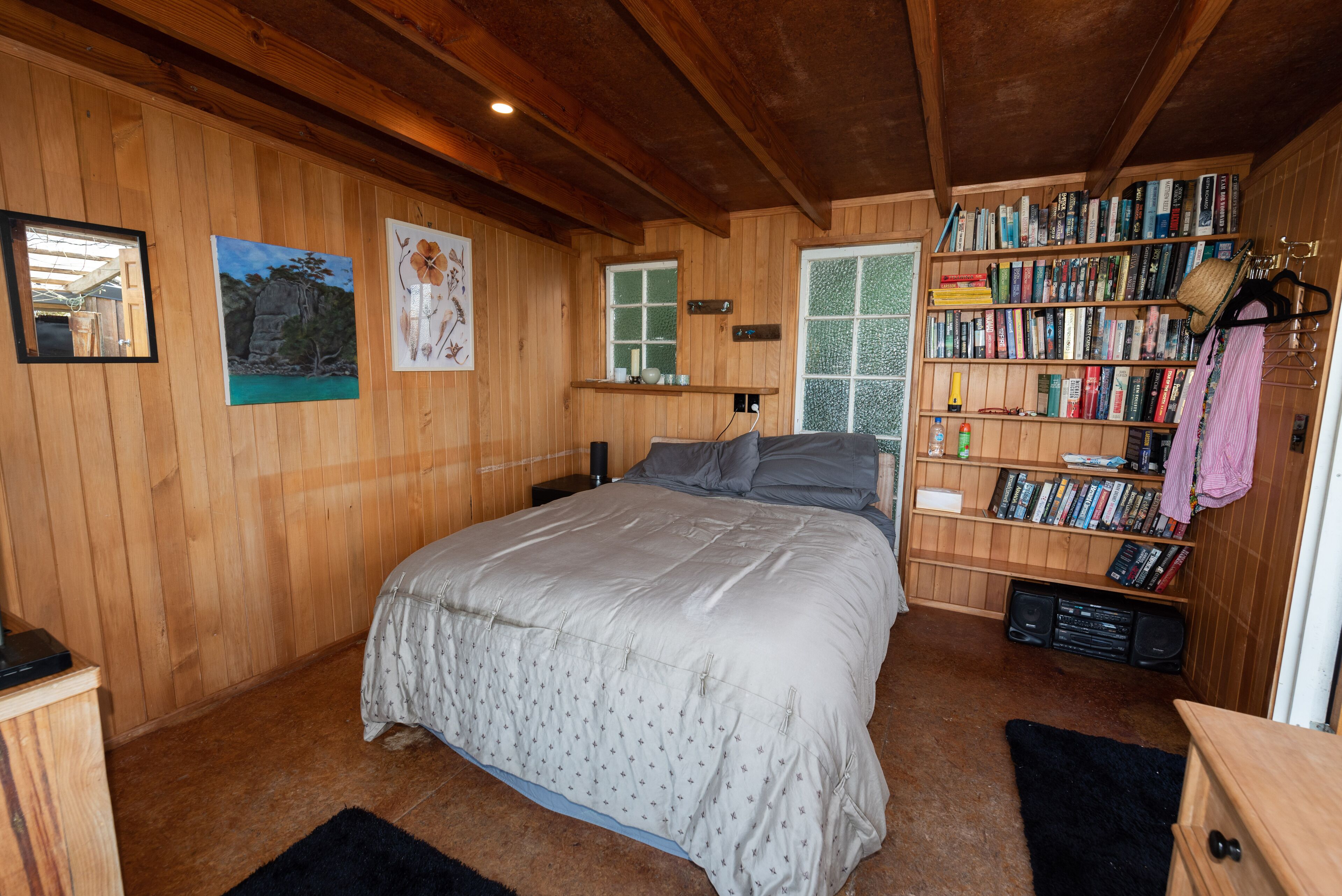 Un dormitorio con paneles de madera, una cama, una estantería y un ventanal.