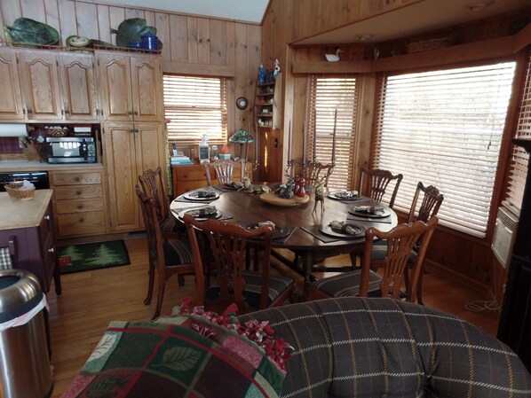 Un comedor acogedor con mobiliario de madera, una mesa de comedor preparada para cuatro personas y una zona de cocina con armarios de madera y un microondas.