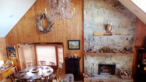 A cozy, wooden interior with a dining area, fireplace, and stone wall. - Breath Taking View of the Highlands of the Roan with Hot Tub and Pool Table (Roan Mountain)
