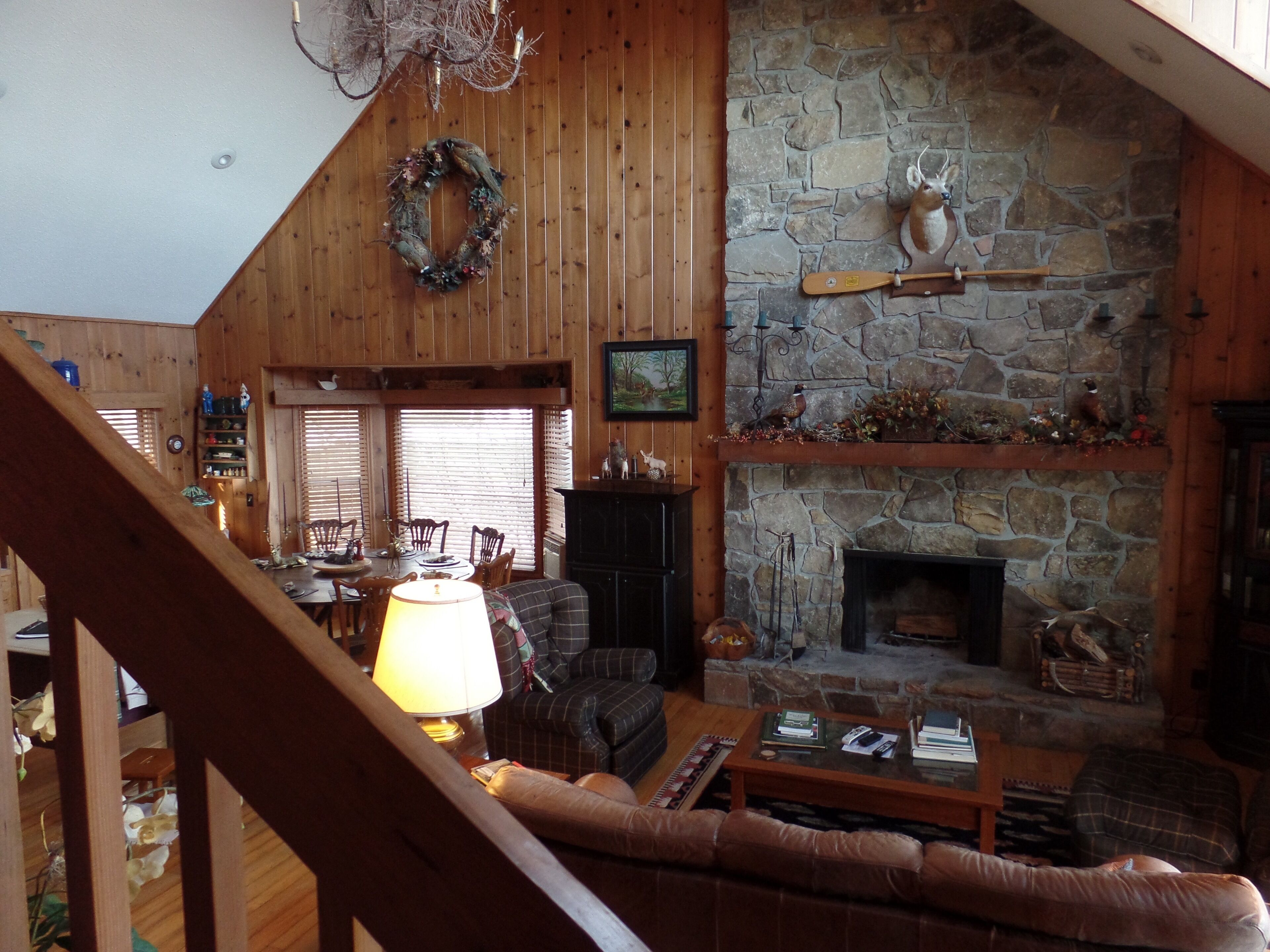 A cozy living room with a stone fireplace, wooden walls, and a dining area with a table and chairs.