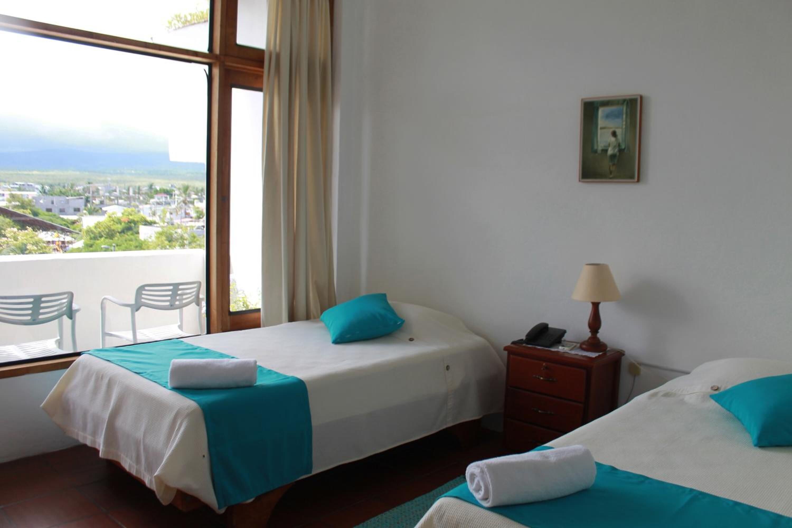 A hotel room with two beds, a window with a view of a town, a small table, and a chair.