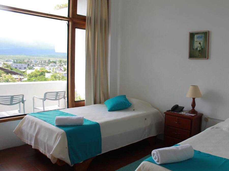 A hotel room with two beds, a window with a view of a town, a small table, and a chair.