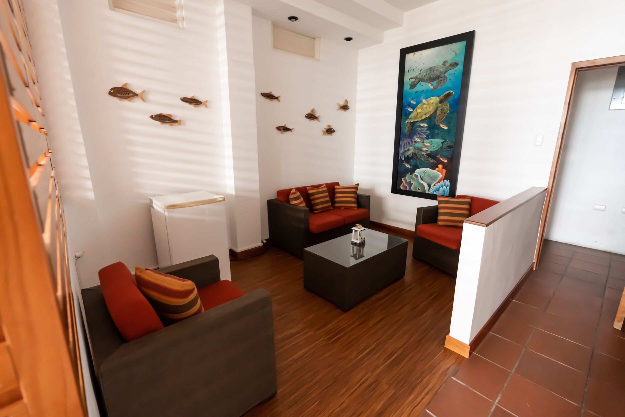 Un salon moderne comprenant un canapé, deux fauteuils, une table basse et un tableau représentant des créatures marines.