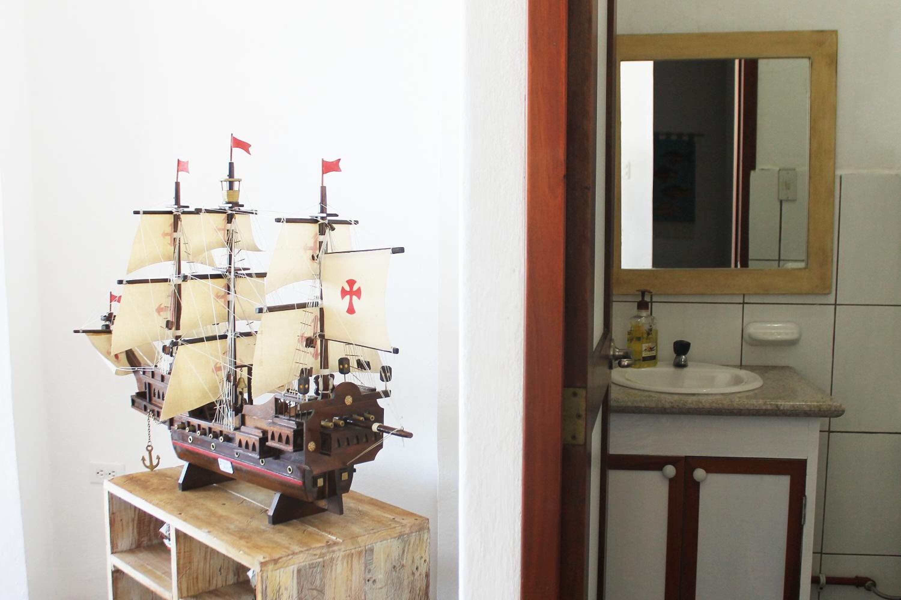 A model ship in a room with a wooden cabinet, a sink, and a mirror above it.