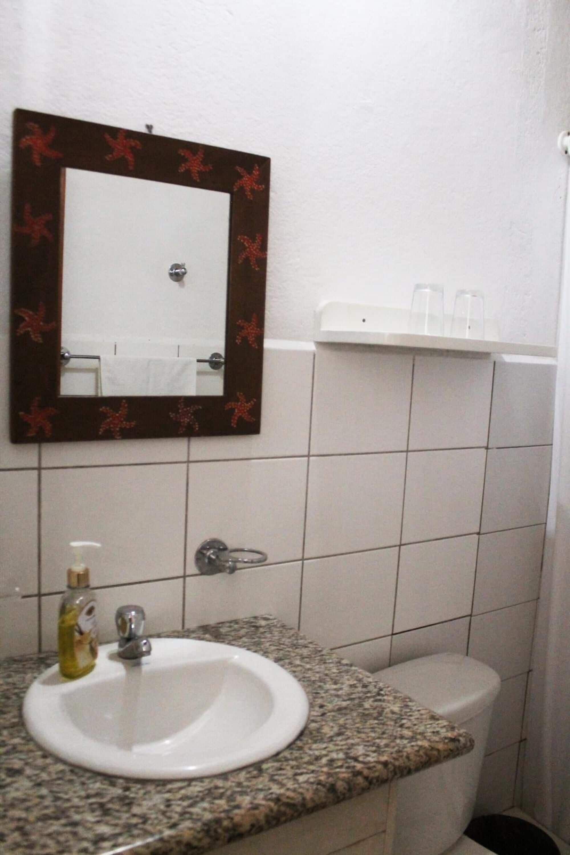 Ein Badezimmer mit einem Waschbecken mit Granitplatte, einem Spiegel mit Zierrahmen, einer Toilette und einem kleinen Regal darüber.