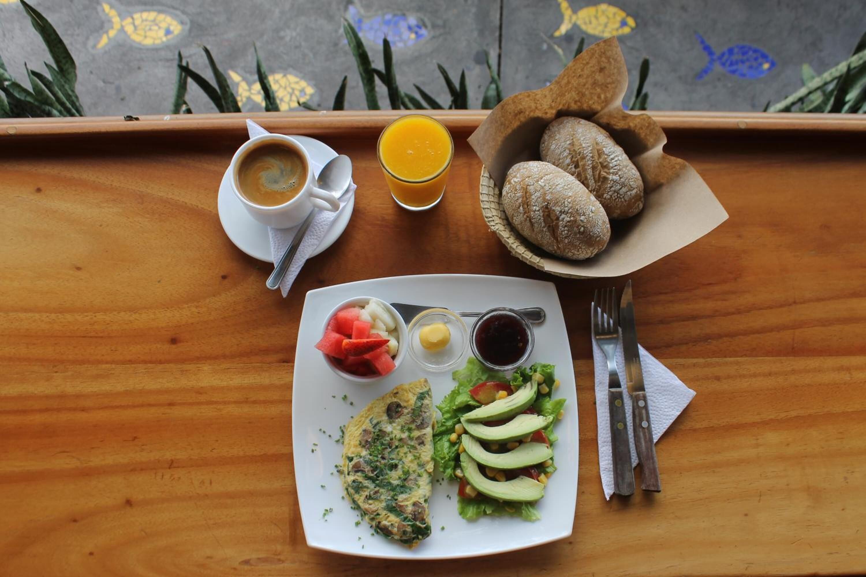 Un plateau avec une tasse de café, un verre de jus d’orange, un panier de pain, une assiette contenant une omelette, une salade et des condiments.