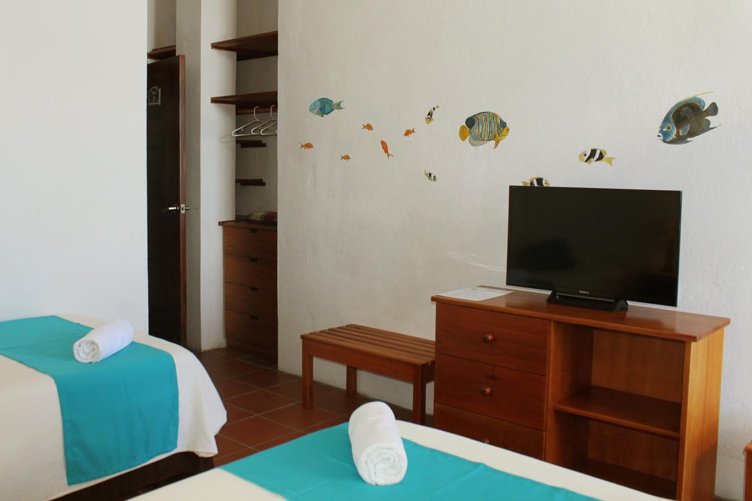 A hotel room with two beds, a TV, a wooden dresser, and a bench.