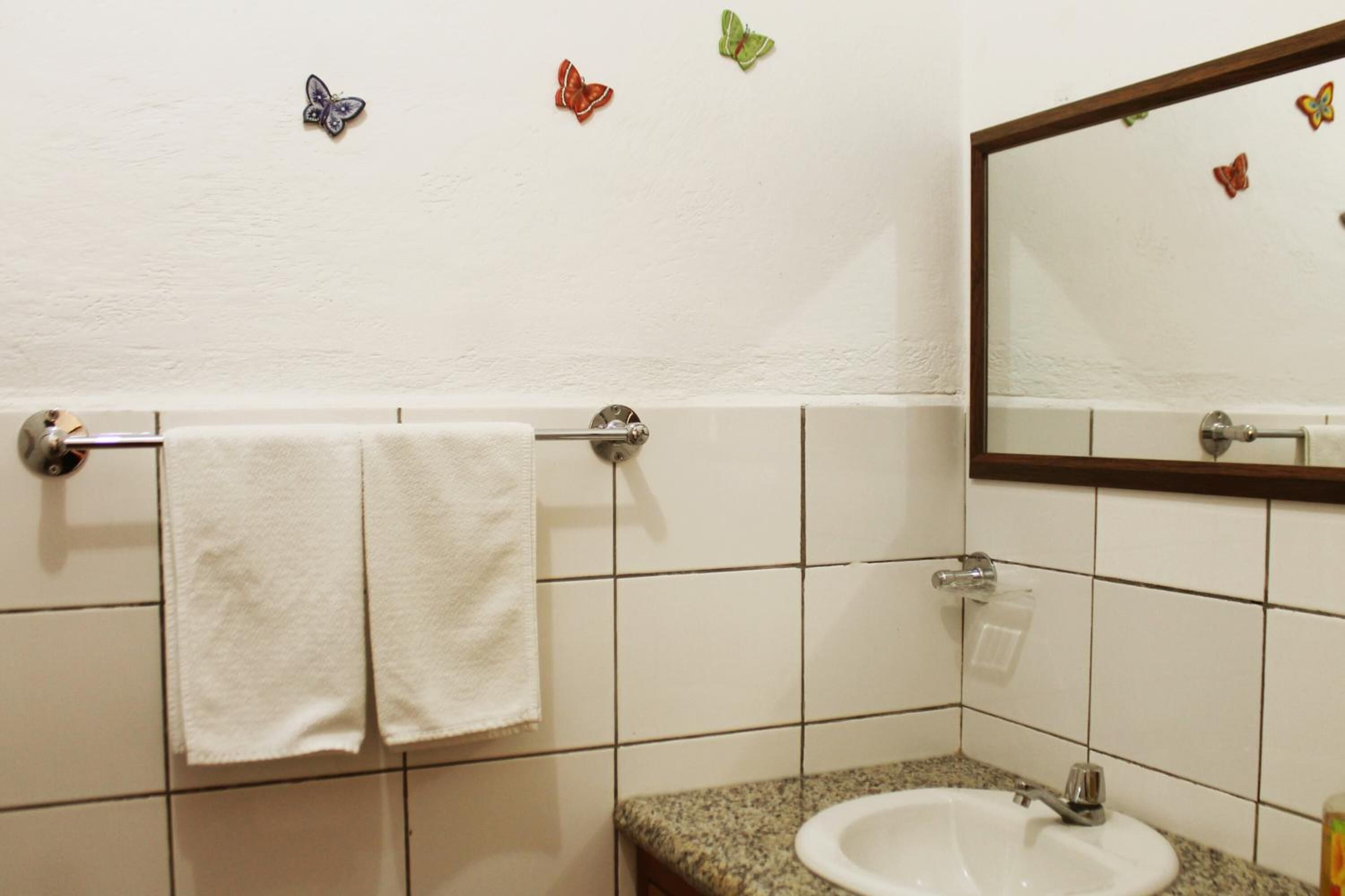 A bathroom with a white sink, a towel rack with two towels, and a mirror with butterfly decals on the wall.