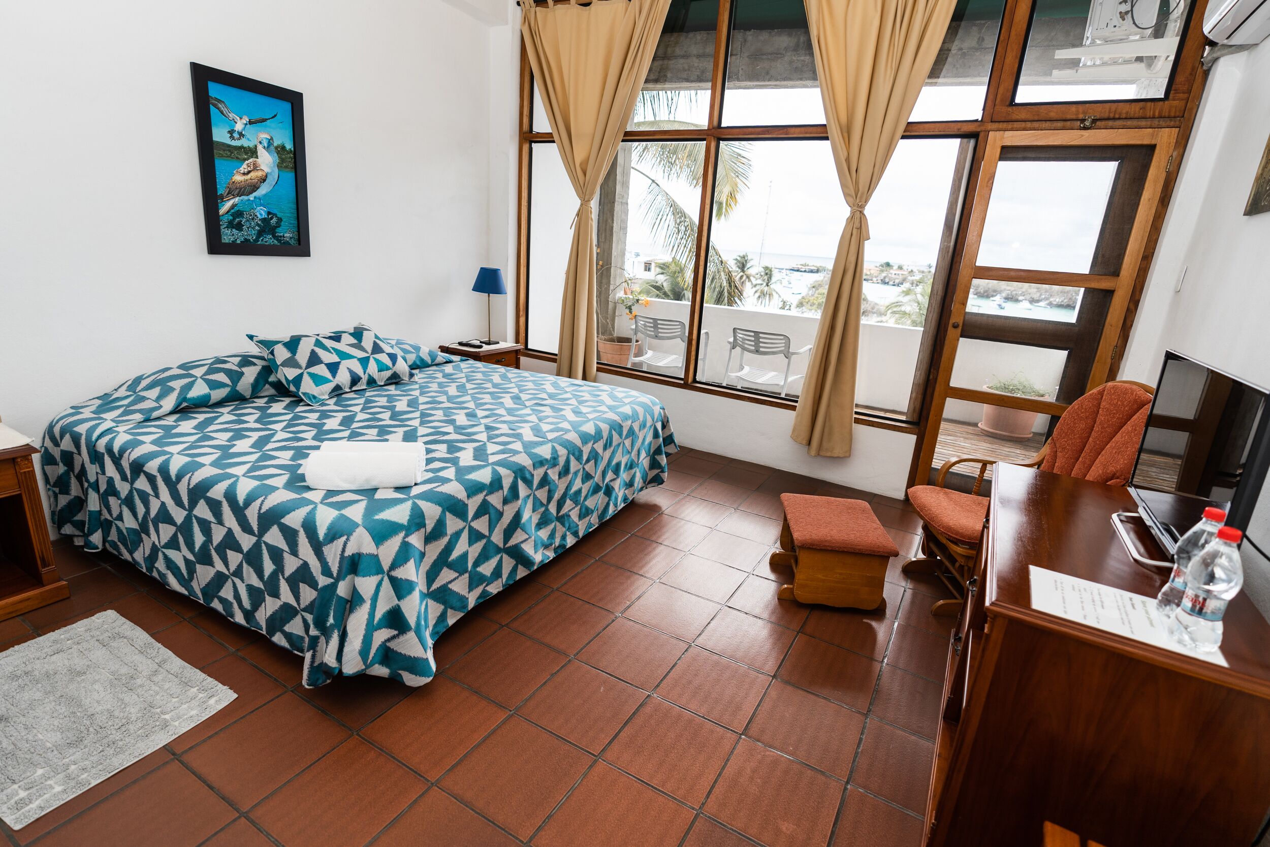 Habitación de hotel con cama, escritorio, silla, ventana con cortinas y vistas al exterior.