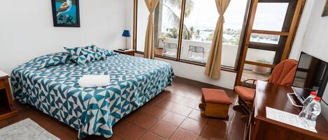 Habitación de hotel con cama, escritorio, silla, ventana con cortinas y vistas al exterior.