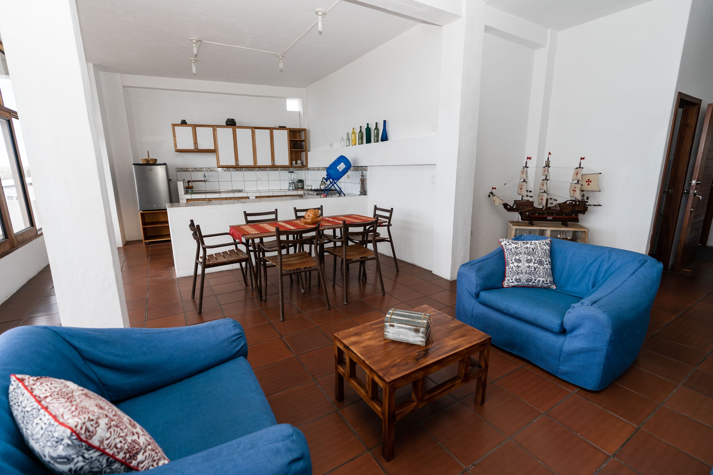 Una sala de estar con sofás azules, una mesa de centro de madera y un comedor con mantel rojo.