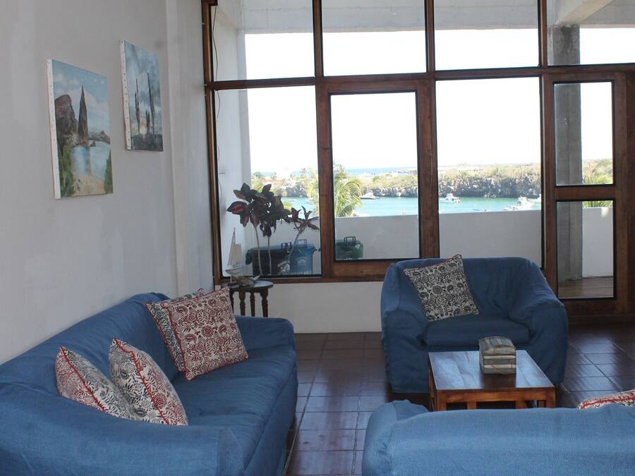 A living room with two blue sofas, a small wooden table, and a large window offering a view of a coastal area.