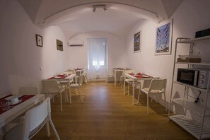 A dining area with white tables and chairs, a microwave, and a shelf with kitchen items. - Casa Rural Julio Vegas (Santiago del Campo)
