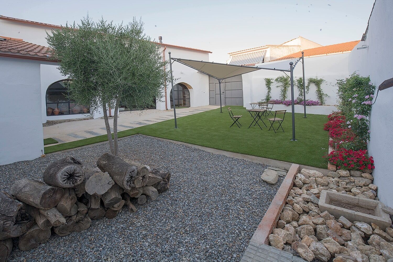 Un patio con un árbol pequeño, un espacio de descanso y un sendero de grava.
