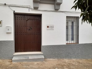 A building with a large wooden door, a small window with metal bars, and a sign indicating 'Casa Rural Julio Vegas'. - Casa Rural Julio Vegas (Santiago del Campo)
