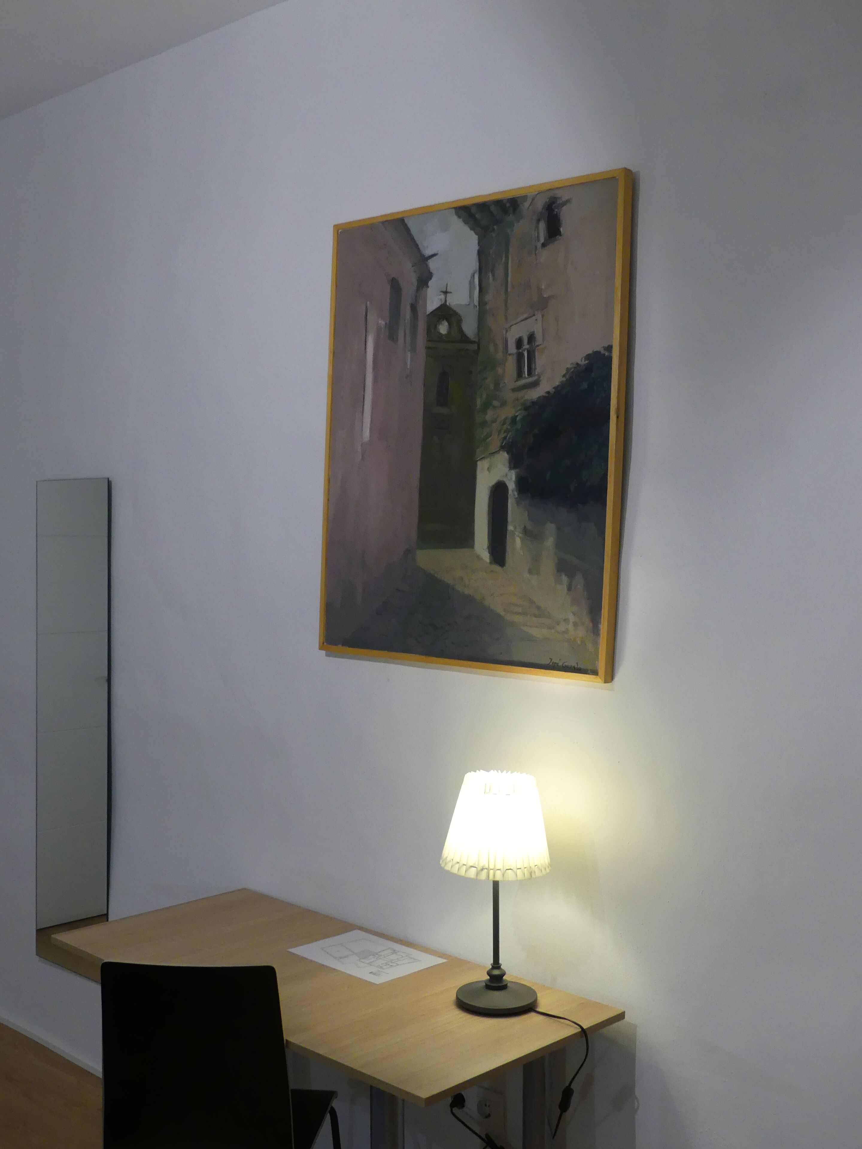 Een kamer met een bureau, een lamp en een schilderij aan de muur.