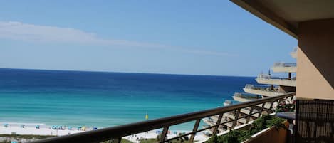 Uma varanda com vista para o oceano, uma piscina e guarda-sóis de praia.