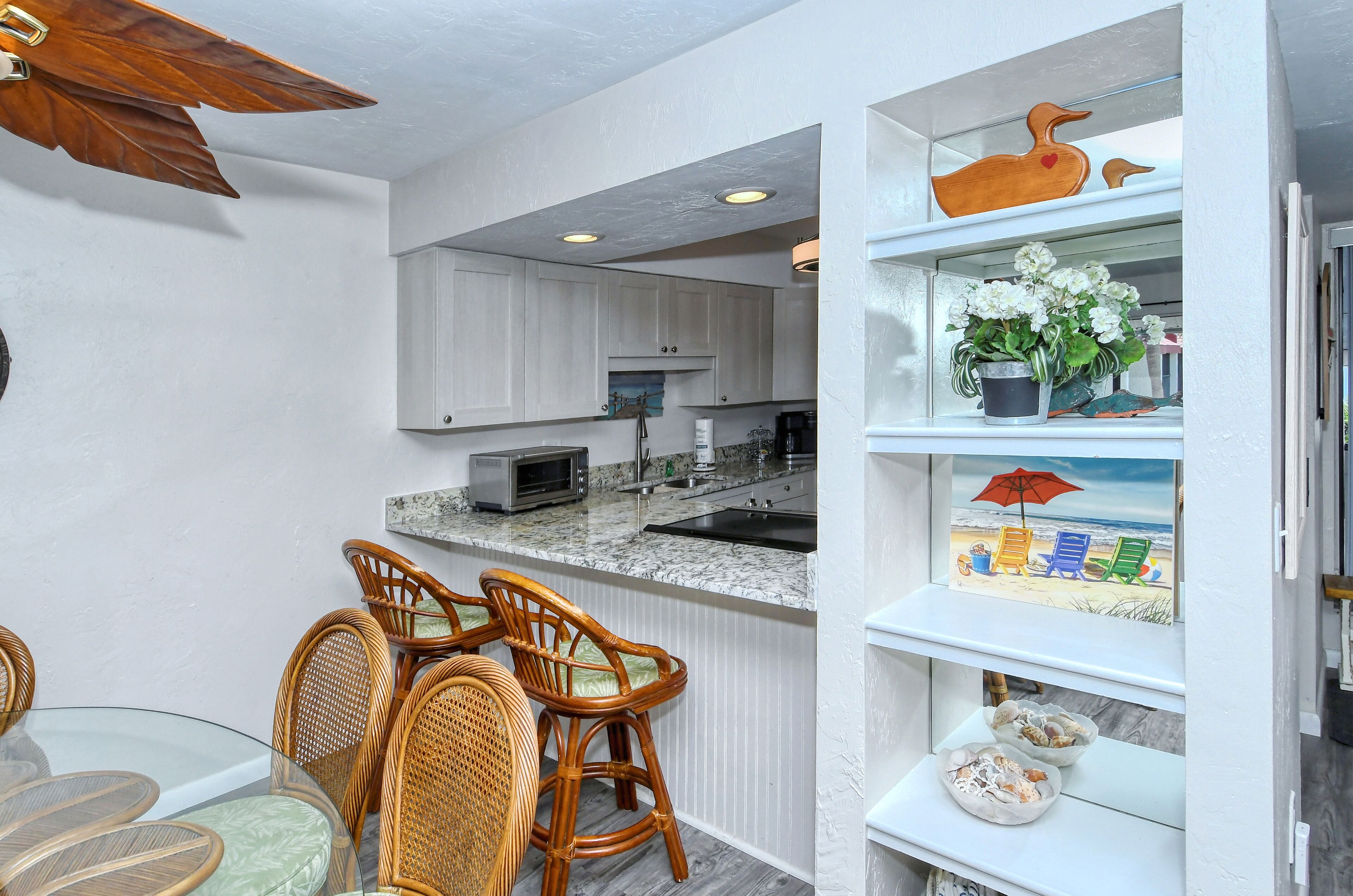 A kitchen with white cabinets, a microwave, and a sink. There are wicker chairs and a glass table.