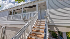 Une maison à deux étages avec un porche à l’avant, un escalier en bois et une antenne parabolique.