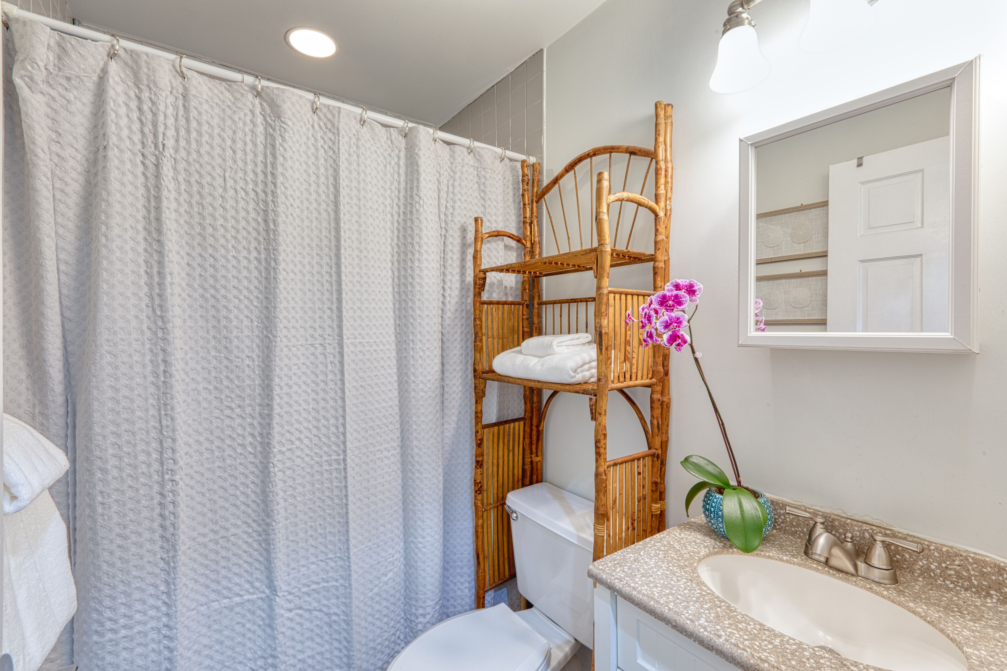 Un baño con cortina de ducha, inodoro, lavabo, espejo y una silla de madera.