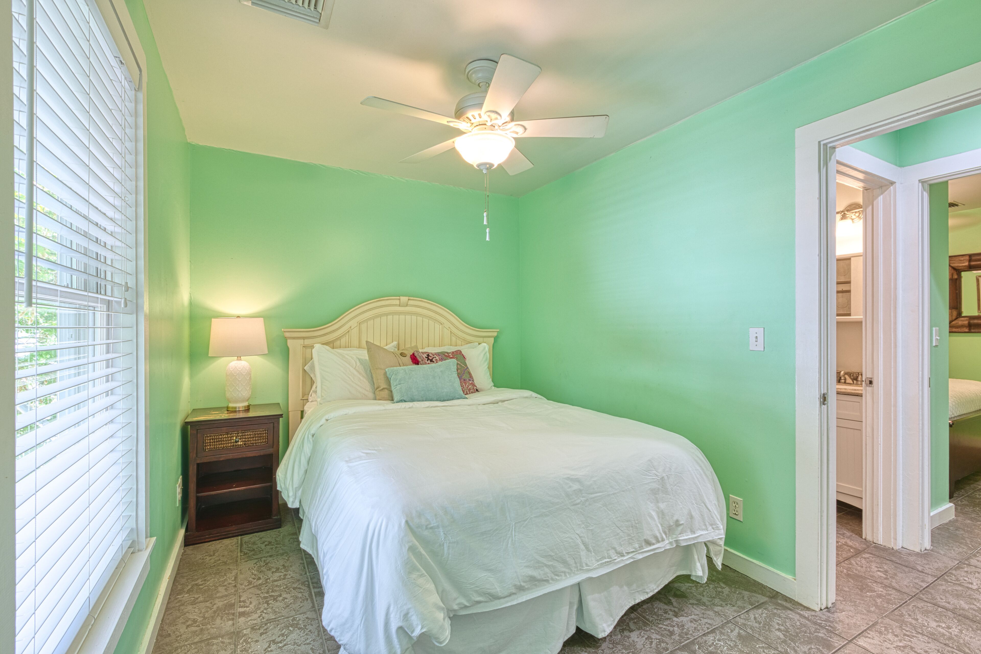 A bedroom with a bed, a nightstand, a ceiling fan, and a window with blinds.