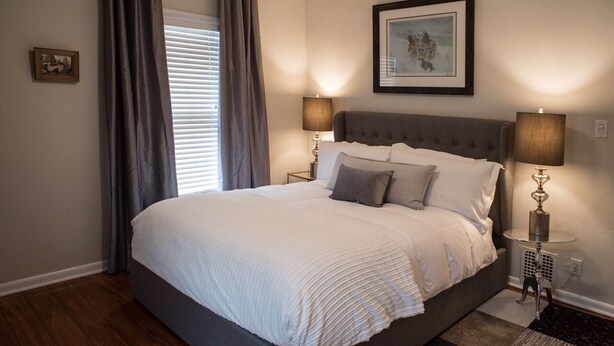 A bedroom with a large bed, two bedside lamps, a framed picture above the bed, and a window with curtains. - Sweet Spot in West Washington Park (Denver)