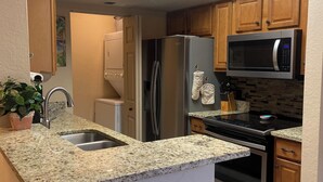 Eine Küche mit Granit Arbeitsplatten, Edelstahlgeräten, Holzschränken und einer integrierten Bar mit gepolsterten Hocker.