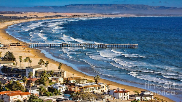 A coastal town with a beach, a pier extending into the ocean, and residential buildings.