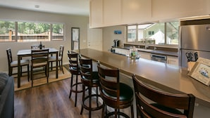 A modern kitchen with a long island, wooden chairs, a dining table, and a refrigerator.