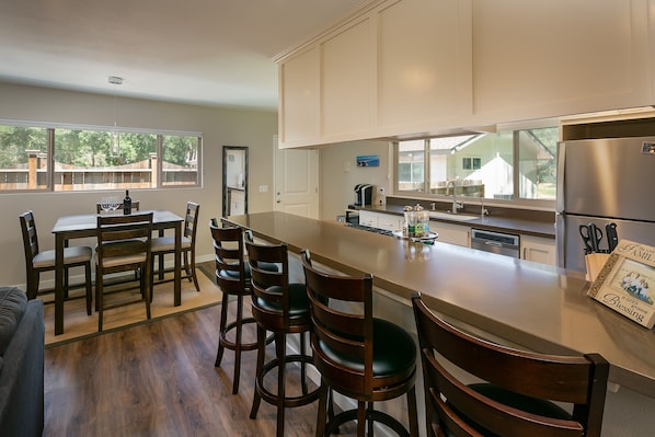 A modern kitchen with a long island, wooden chairs, a dining table, and a refrigerator.