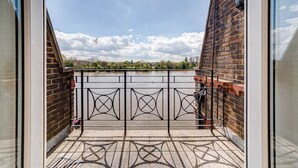 A balcony with a patterned floor, a metal gate, and a view of a body of water and greenery. - River View, London Zone 2 Hammersmith, 2 Bedroom / 2 Bath (London)
