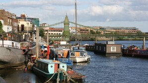 A harbor with boats docked, a bridge in the background, and buildings along the riverbank. - River View, London Zone 2 Hammersmith, 2 Bedroom / 2 Bath (London)