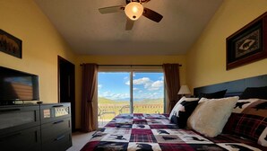 Un dormitorio con una cama grande, un televisor en una cómoda y vistas al exterior.
