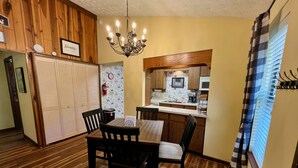 Cocina compacta con armarios de madera, un microondas y un lavamanos. Hay una zona de comedor con una mesa y sillas.