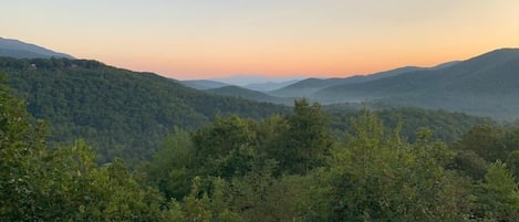 Un paisaje montañoso con densa vegetación forestal y una plataforma de madera para observar el panorama.