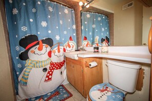 A bathroom with a snowman-themed shower curtain, a wooden cabinet, and a toilet.