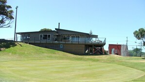 A modern building with a flat roof and large windows, situated on a grassy slope. - Beach Villa One -  Family Unit (Riversdale)