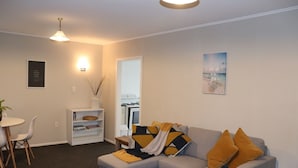 A modern living room with a grey sofa, yellow cushions, a small table, and a bookshelf. - Beach Villa One -  Family Unit (Riversdale)