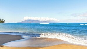 Una spiaggia con acque cristalline, una riva sabbiosa e una montagna in lontananza.