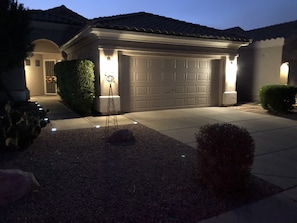 A residential garage with a tiled roof, a gravel driveway, and a well-lit entrance.