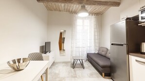 A compact kitchen with a modern refrigerator, a dining table with a metal bowl, a gray sofa, and a ceiling with exposed beams. - Great brand new 1 bedroom apartment in the center of old Antibes (Antibes)