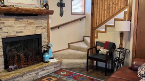Ein Wohnzimmer mit Kamin, Treppe, einer Ledersofa und einem gemusterten Teppich.